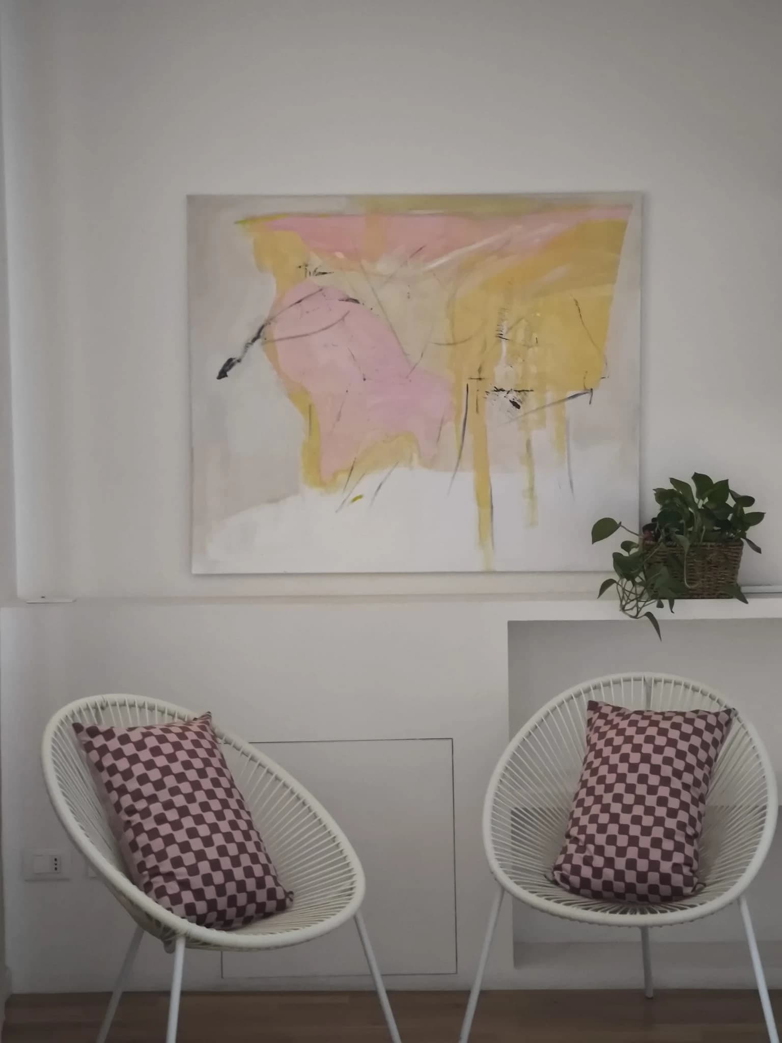 A pink and yellow canvas above a ledge, with two white wire chairs below